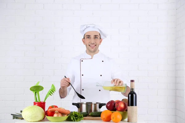 Chef à mesa com diferentes produtos e utensílio na cozinha no fundo da parede branca — Fotografia de Stock