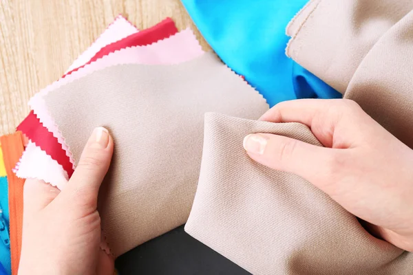 Échantillons de tissu coloré dans les mains féminines sur fond de table en bois — Photo