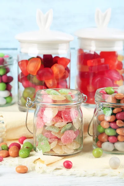 Caramelos multicolores en frascos de vidrio sobre fondo de madera de color — Foto de Stock