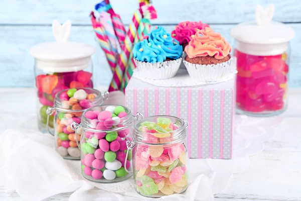 Multicolor candies in glass jars and cupcakes on color wooden background — Stock Photo, Image