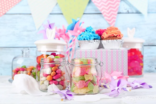 Bonbons multicolores dans des bocaux en verre et des cupcakes sur fond en bois de couleur — Photo