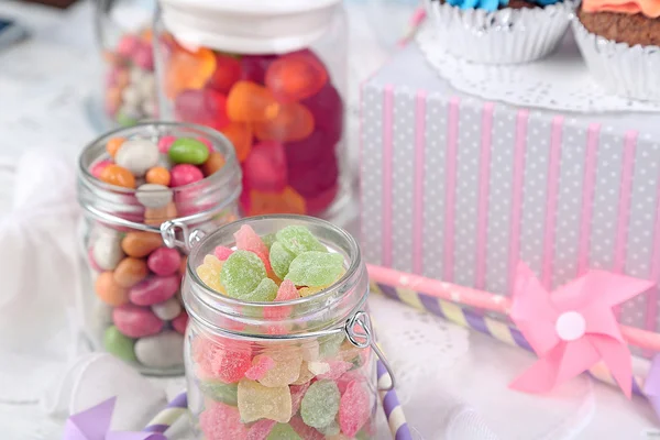 Multicolor candies in glass jars and cupcakes on color wooden background — Stock Photo, Image