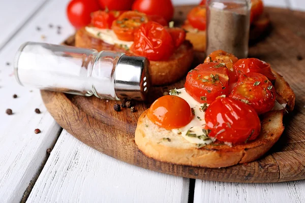 Rebanadas de pan tostado blanco con mantequilla y tomates enlatados sobre fondo de tablones de madera de color — Foto de Stock
