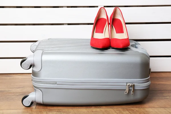 Grauer Koffer mit Frauenschuhen auf dem Boden auf weißen Planken Hintergrund — Stockfoto