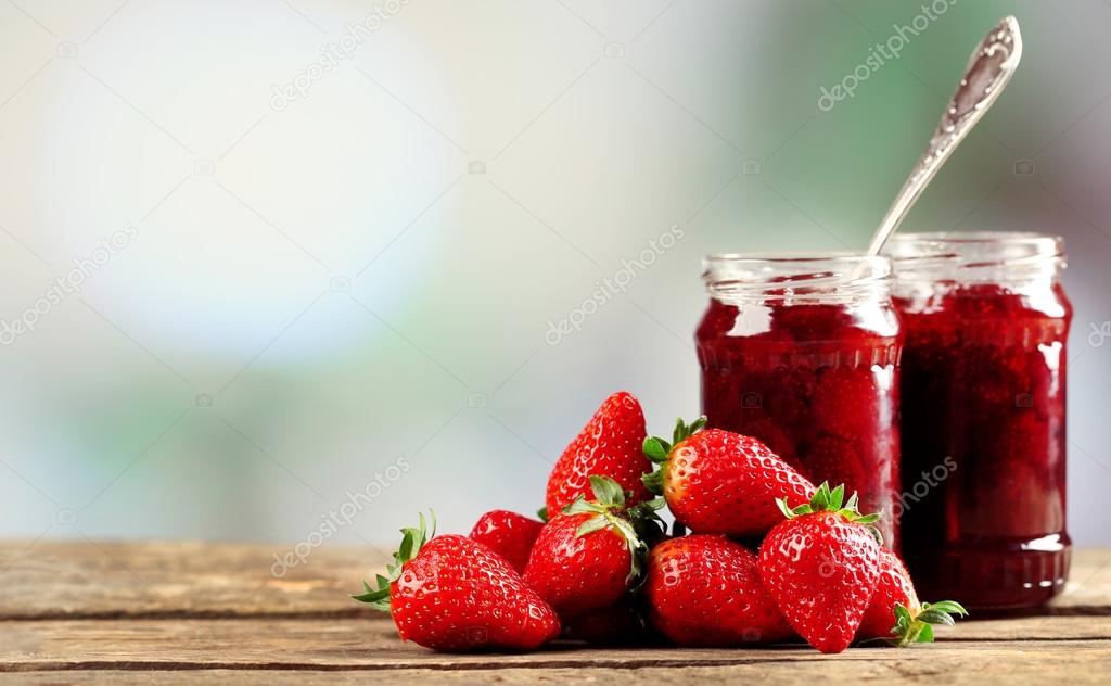 Jars of strawberry jam with berries on table on bright background