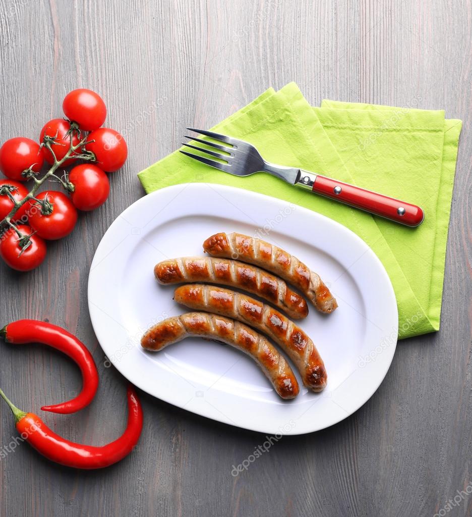 Grilled sausages on plate with vegetables on table close up