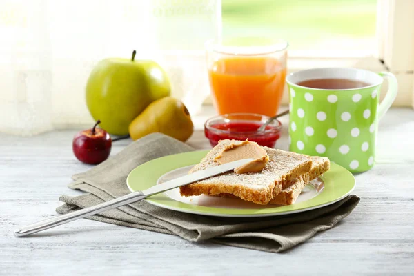 Toasts with peanut butter on plate with cup of tea and juice on light background — Stock Photo, Image