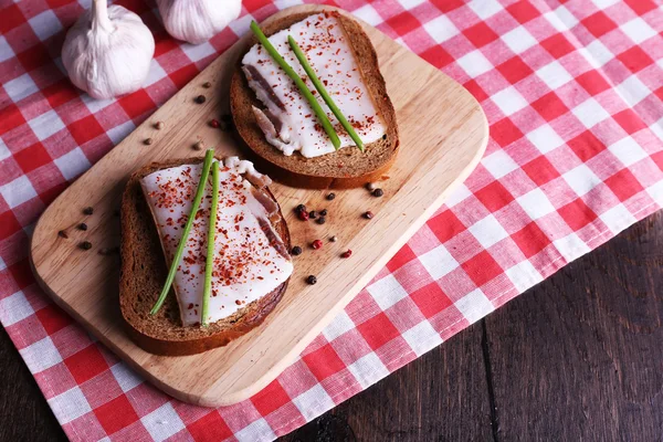 Сэндвичи с салом на доске и чесноком на столе крупным планом — стоковое фото