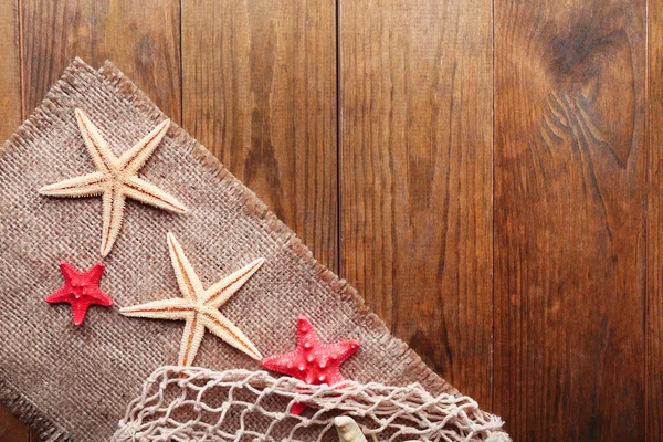 Sea stars on sackcloth on wooden background — Stock Photo, Image