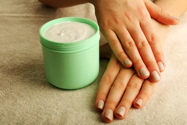 Manos femeninas con tarro de crema sobre fondo de tela —  Fotos de Stock