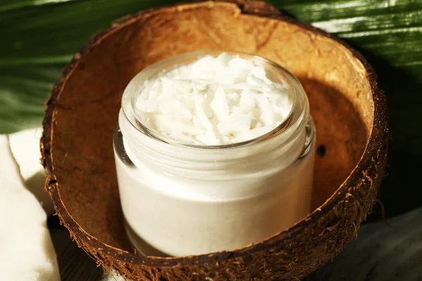 Aceite de coco fresco en botella de vidrio y hoja verde sobre fondo de mesa de madera — Foto de Stock