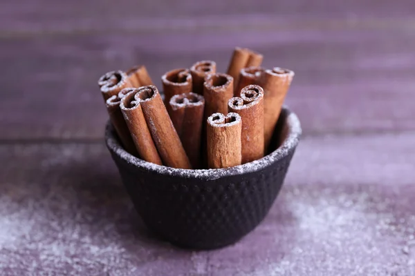 Palitos de canela en un tazón pequeño con azúcar en polvo sobre fondo de mesa de madera de color — Foto de Stock