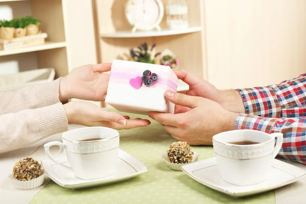 Mani femminili e maschili con tazze di tè e scatola regalo su sfondo interno domestico — Foto Stock