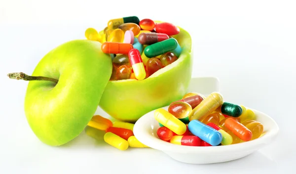 Maçã e comprimidos coloridos, isolados em branco — Fotografia de Stock