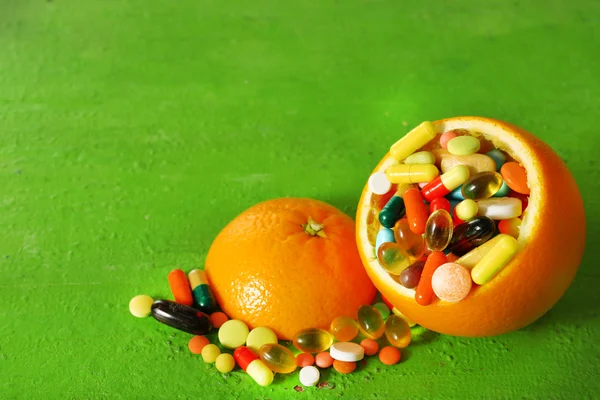 Frutas de laranja e pílulas coloridas, em fundo de madeira — Fotografia de Stock