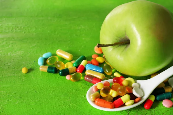 Apple and colorful pills, on color wooden background — Stock Photo, Image