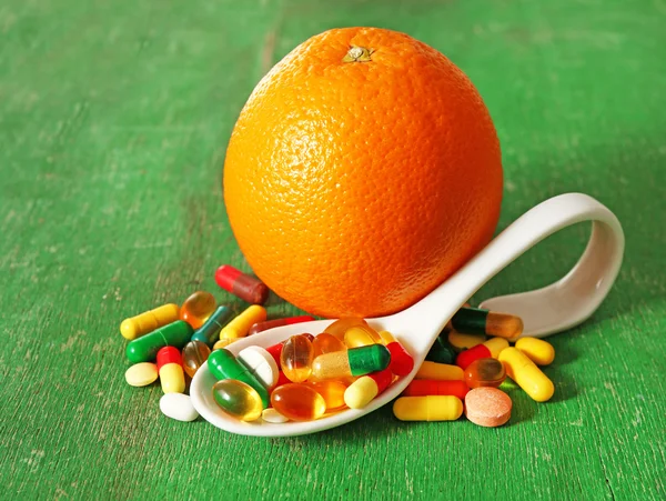 Frutta arancione e pillole colorate, su sfondo di legno — Foto Stock