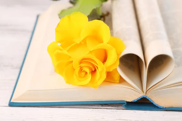 Open book with shape of heart from pages and yellow rose on wooden table, closeup — Stock Photo, Image