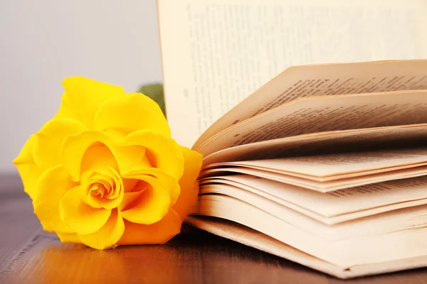 Book with yellow rose on wooden table on light background