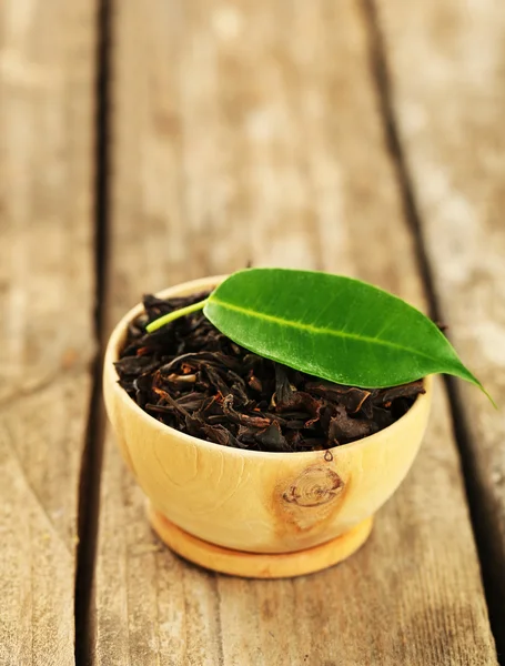 Té negro con hoja en tazón sobre mesa de madera vieja — Foto de Stock