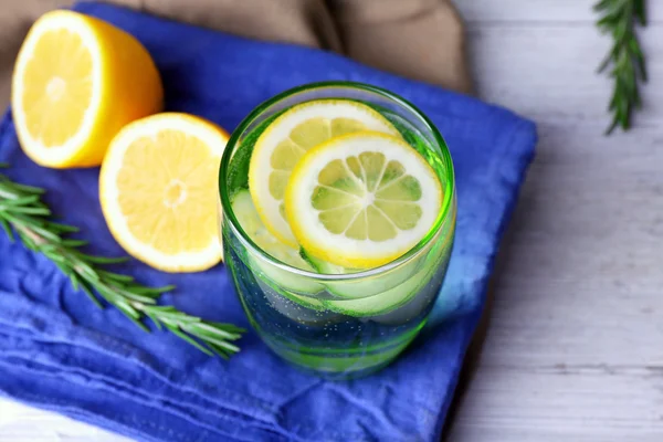 Fresh water with lemon and cucumber in glassware on napkin on wooden table, closeup — Stock Photo, Image