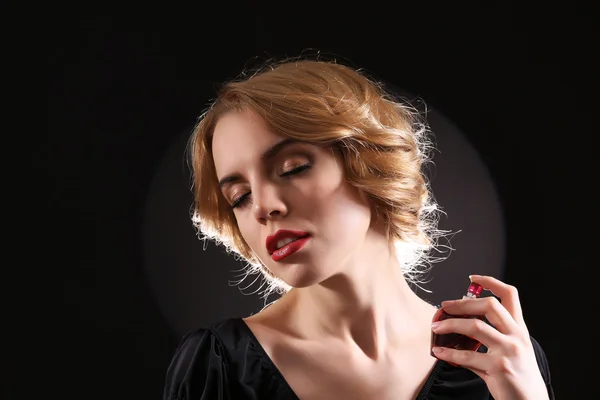 Mooie jonge vrouw met parfumfles op zwarte achtergrond — Stockfoto