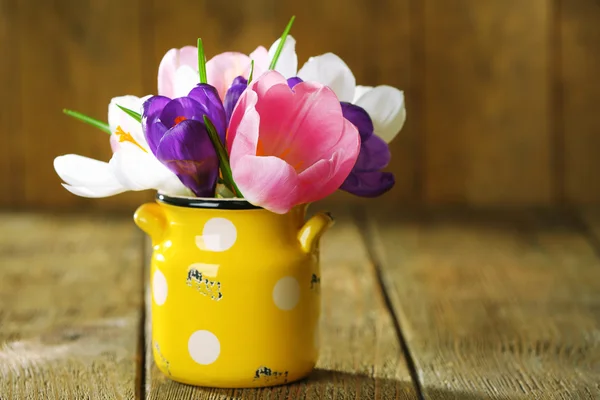 Beautiful spring flowers in yellow pot on wooden background — Stock Photo, Image