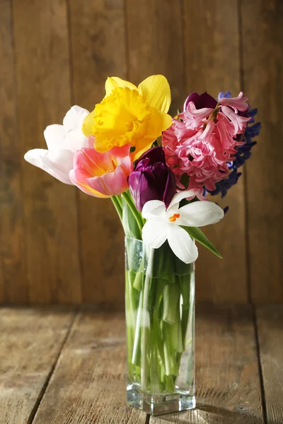 Bellissimi fiori primaverili in vaso di vetro su sfondo di legno — Foto Stock