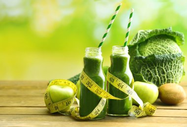 Meyve ve sebze ahşap masa ve parlak arka plan ile cam şişelerde yeşil taze sağlıklı meyve suları