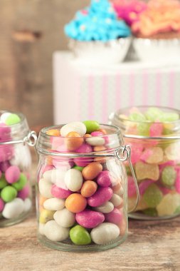 Cam Kavanoz ve cupcakes ahşap arka plan üzerinde çok renkli şekerler