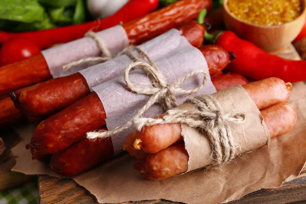 Assortimento di salsicce sottili, senape in ciotola e spezie su tagliere, su fondo di legno — Foto Stock