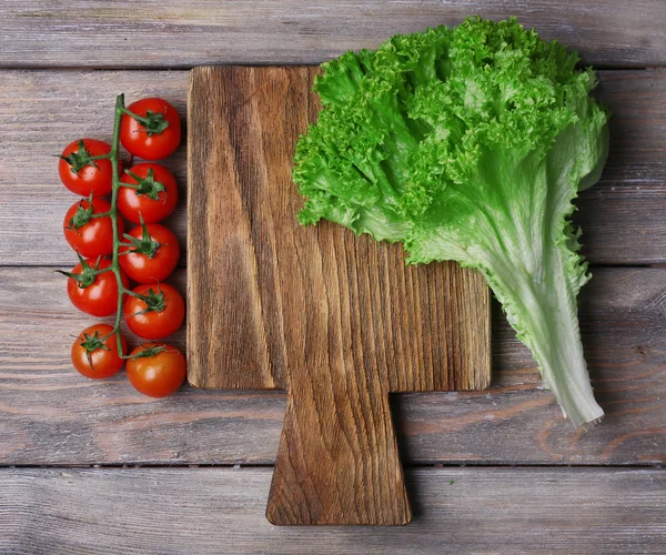 Cutting board with cherry tomatoes and lettuce on rustic wooden planks background — Stock Photo, Image