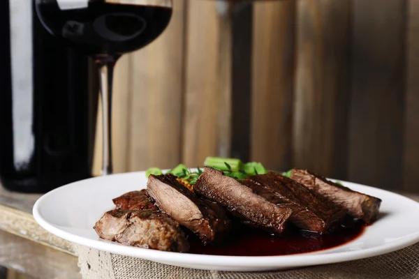 Steak with wine sauce on plate and bottle of wine on wooden background — Stock Photo, Image