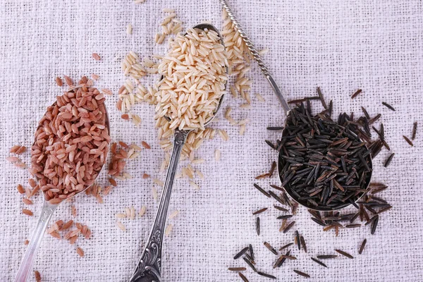 Diferentes tipos de arroz en cucharas sobre fondo de tela —  Fotos de Stock