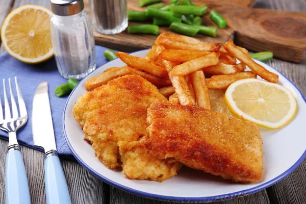 Breaded fried fish fillets and potatoes with asparagus and sliced lemon on plate and wooden planks background — Stock Photo, Image