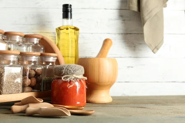 Diverse spezie verdure in scatola in bottiglie di vetro su stand con utensili e in scatola su tavolo di legno e tavole di sfondo — Foto Stock