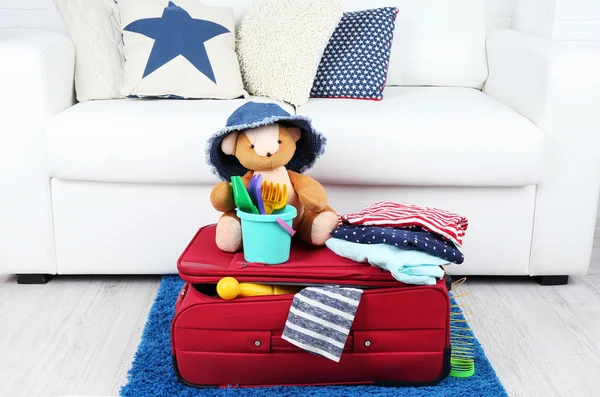 Suitcase packed with clothes and child toys on fur rug and white sofa background — Stock Photo, Image