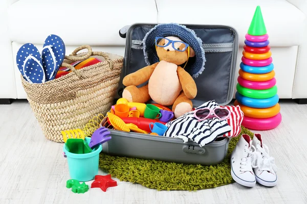 Suitcase packed with clothes and child toys on fur rug and white sofa background — Stock Photo, Image