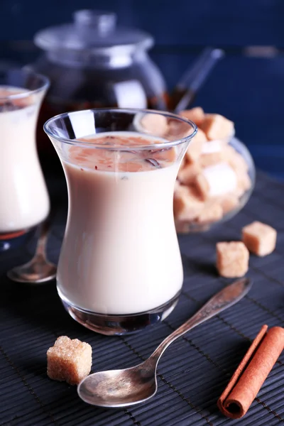 Teh hitam dengan susu dalam gelas dan teko teh dengan lump gula di tikar bambu dan latar belakang papan kayu warna — Stok Foto