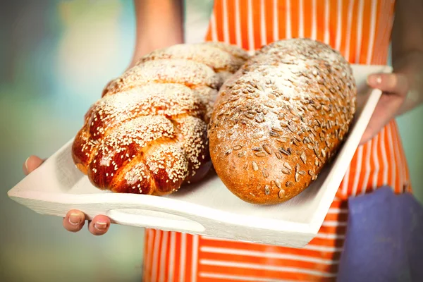 Traditional bread in female hands on wooden tray on light blurred background — Stock Photo, Image