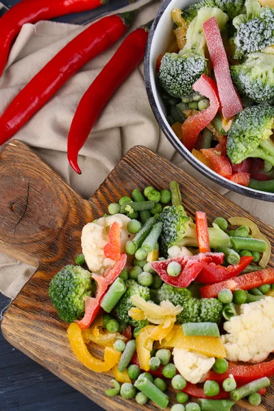 Verduras congeladas sobre tabla de cortar, sobre servilleta, sobre fondo de mesa de madera — Foto de Stock