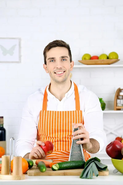 Человек за столом с различными продуктами и посудой на кухне на белом фоне стены — стоковое фото