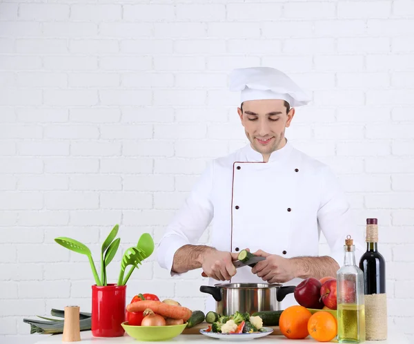 Kock på bord med olika produkter och redskapen i köket på vit vägg bakgrund — Stockfoto
