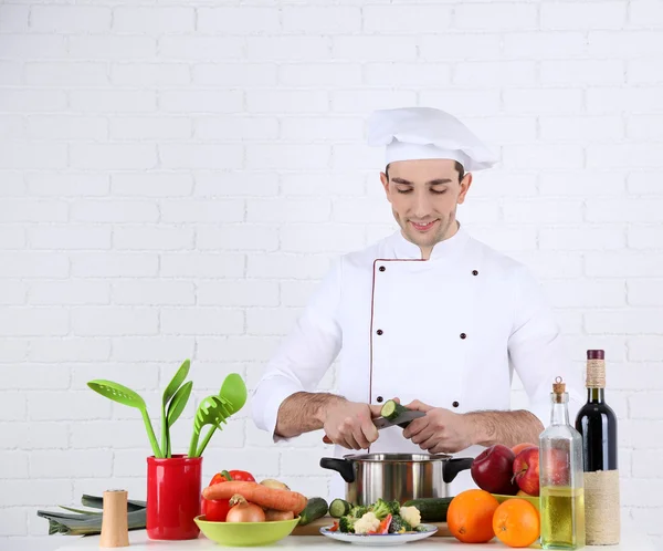 Chef a tavola con diversi prodotti e utensili in cucina su fondo bianco a parete — Foto Stock