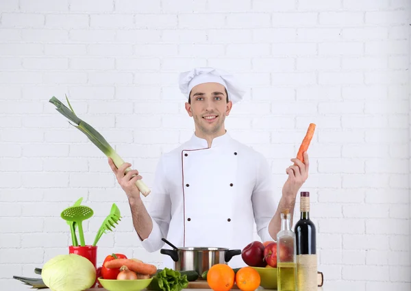 Kock på bord med olika produkter och redskapen i köket på vit vägg bakgrund — Stockfoto