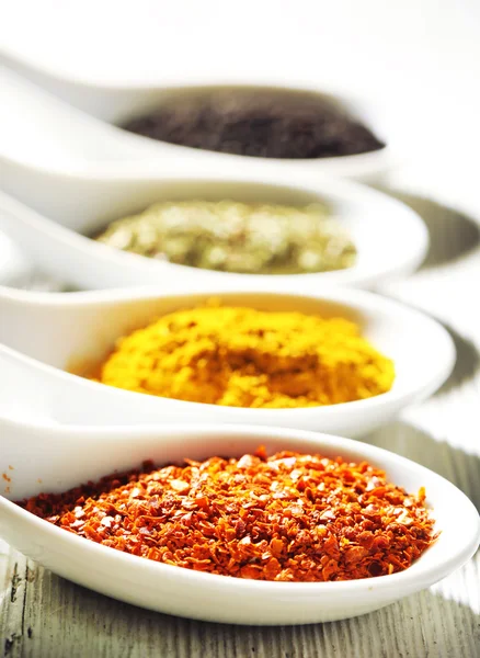 Different kinds of spices in ceramics spoons, close-up, on wooden background — Stock Photo, Image