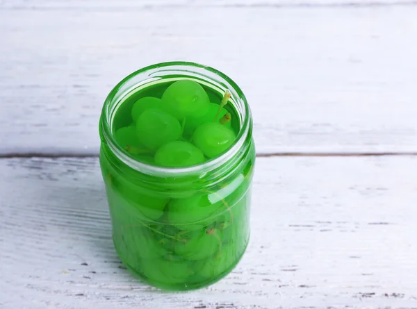 Homemade jar of green maraschino cherry on color wooden planks background