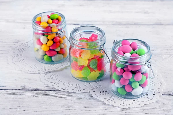 Multicolor candies in glass jars on color wooden background — Stock Photo, Image