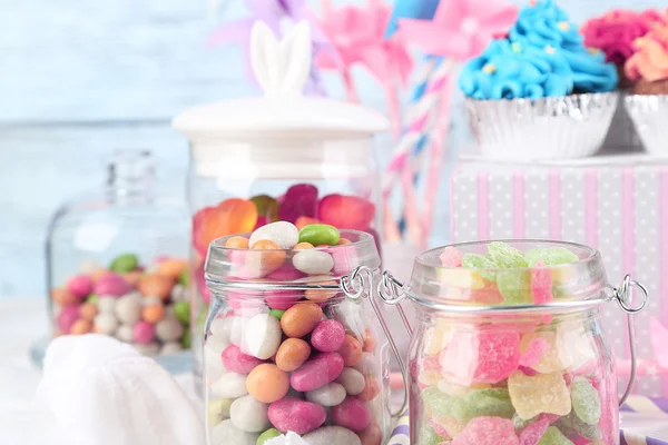 Bonbons multicolores dans des bocaux en verre et des cupcakes sur fond en bois de couleur — Photo