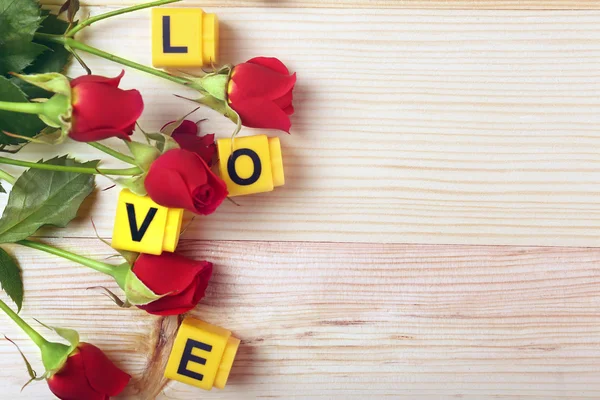 Beautiful roses with word LOVE on wooden background — Stock Photo, Image